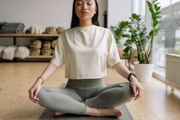Une femme assise en position du lotus les yeux fermés pratique la méditation pour maigrir grâce au yoga en studio.