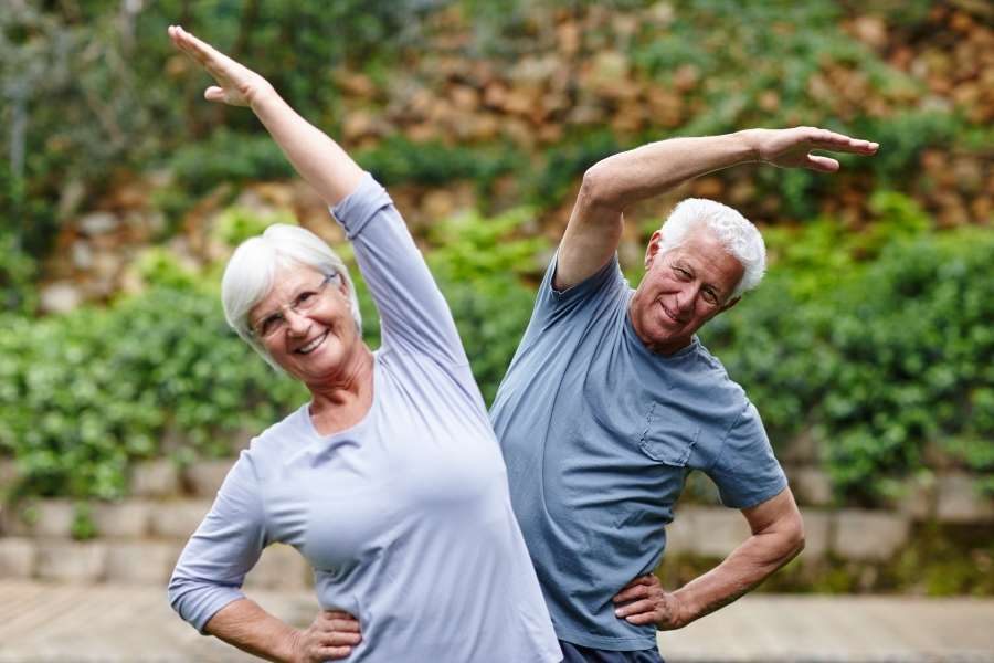 Un couple d'aînés souriants s'étire en plein air lors d'une séance de yoga pour les seniors.