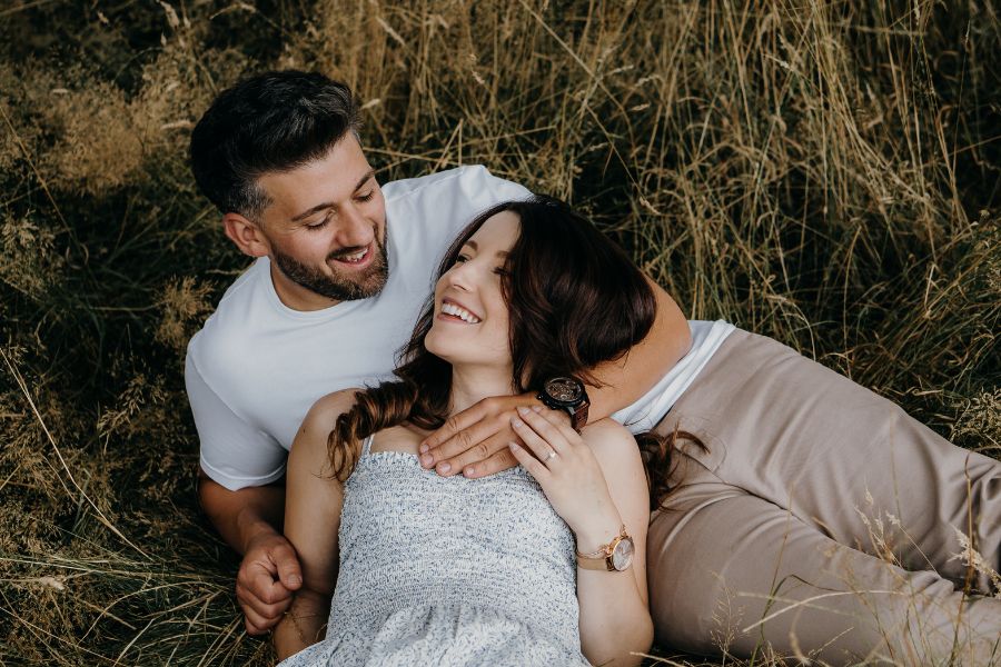 Un couple complice allongé dans l'herbe haute, partageant un moment de complicité pour dépasser la peur du regard.