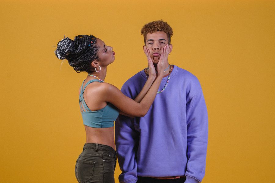 Une femme tenant le visage de son partenaire en riant devant un fond jaune, illustrant l'importance de dépasser la peur du regard des autres.