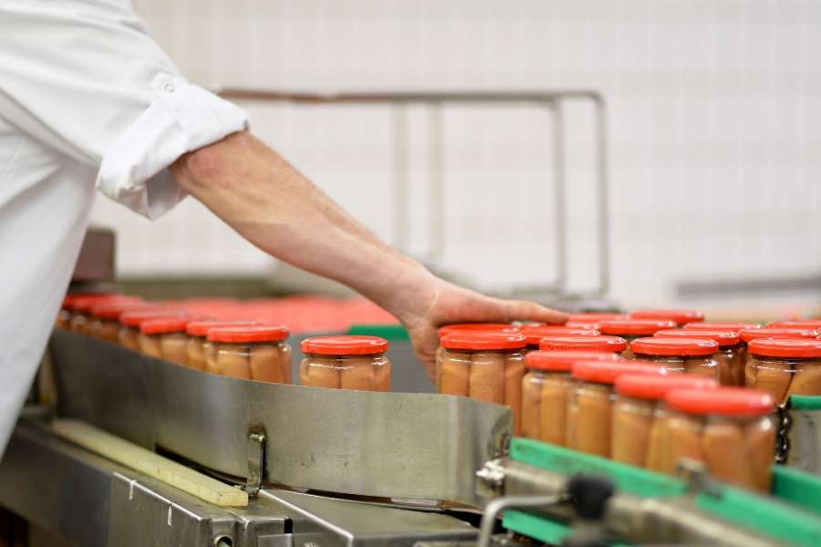 Un opérateur en tenue blanche contrôlant des bocaux de saucisses sur une chaîne de production dans des usines alimentaires.